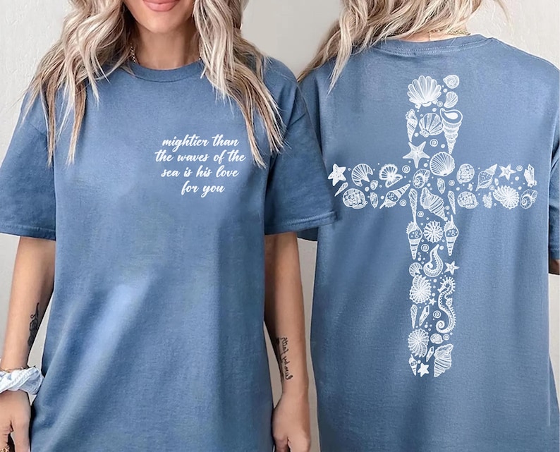 A woman wearing a blue t-shirt with a white cross design and text on the front and back.