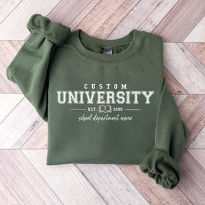 May include: An olive green crewneck sweatshirt featuring white screen-printed text that reads CUSTOM UNIVERSITY, EST. 1890 with a small book icon in the center, and the words school department name written in a cursive script font below.