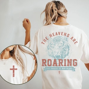 A woman wearing a white t-shirt with a graphic design of a tiger and the text "The heavens are roaring" printed on it.