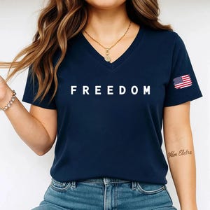A woman wearing a navy blue t-shirt with the word "FREEDOM" printed on it, standing against a white background.