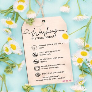 a wooden tag with instructions for washing clothes, placed against a background of white and yellow flowers.