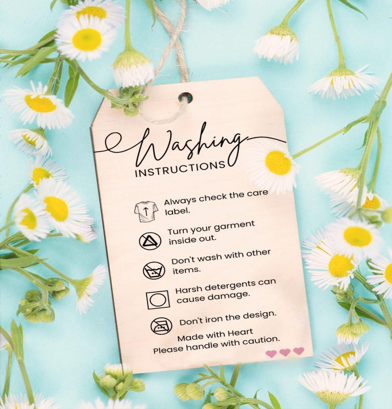 a wooden tag with instructions for washing clothes, placed against a background of white and yellow flowers.