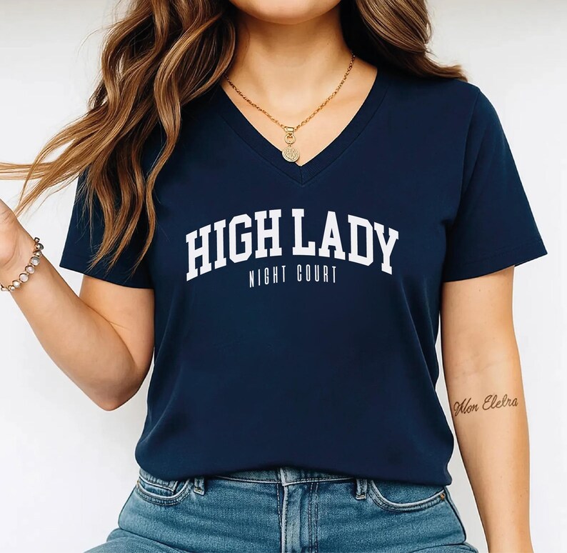 A woman wearing a navy blue t-shirt with the text "HIGH LADY NIGHT COURT" printed on it.