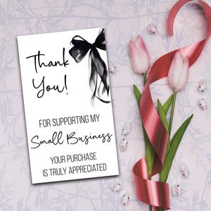 a white card with a black ribbon and pink tulips, along with a red ribbon and small white flowers, all arranged on a floral background.