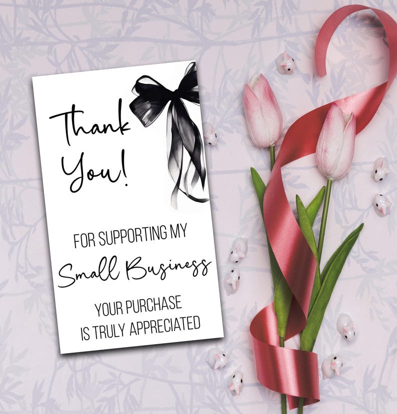 a white card with a black ribbon and pink tulips, along with a red ribbon and small white flowers, all arranged on a floral background.