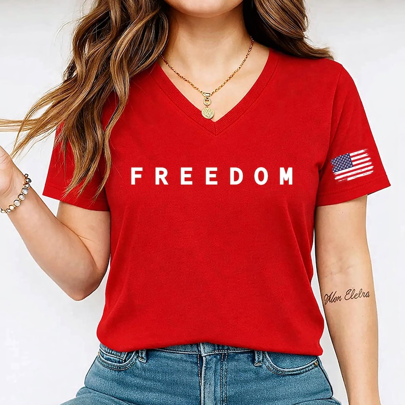 A woman wearing a red t-shirt with the word "FREEDOM" printed on it, along with a necklace and a tattoo on her arm.