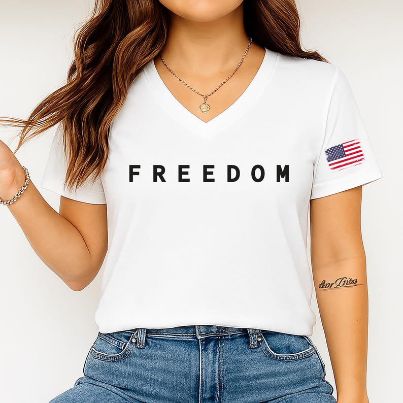 A woman wearing a white t-shirt with the word "FREEDOM" printed on it, along with a necklace and a tattoo on her arm.