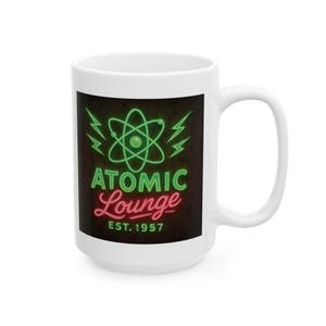 May include: White ceramic mug featuring the "Atomic Lounge" logo in green and red neon-style lettering. The design includes an atom symbol and lightning bolts, with "EST. 1957" below. The mug has a large handle.