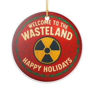 Peut inclure: Ornement de Noël rond avec un fond rouge et l'inscription "WELCOME TO THE WASTELAND HAPPY HOLIDAYS" en crème. Il présente un symbole de radiation jaune et noir au centre et une ficelle dorée pour l'accrocher.
