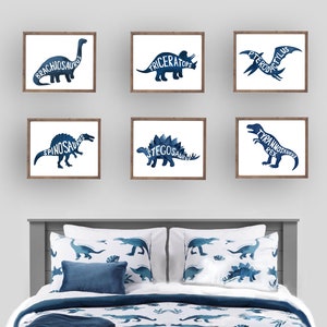 May include: Six framed prints of blue dinosaur silhouettes with the dinosaur's name written inside the silhouette. The prints are arranged in two rows of three on a white wall above a bed with blue and white dinosaur bedding.