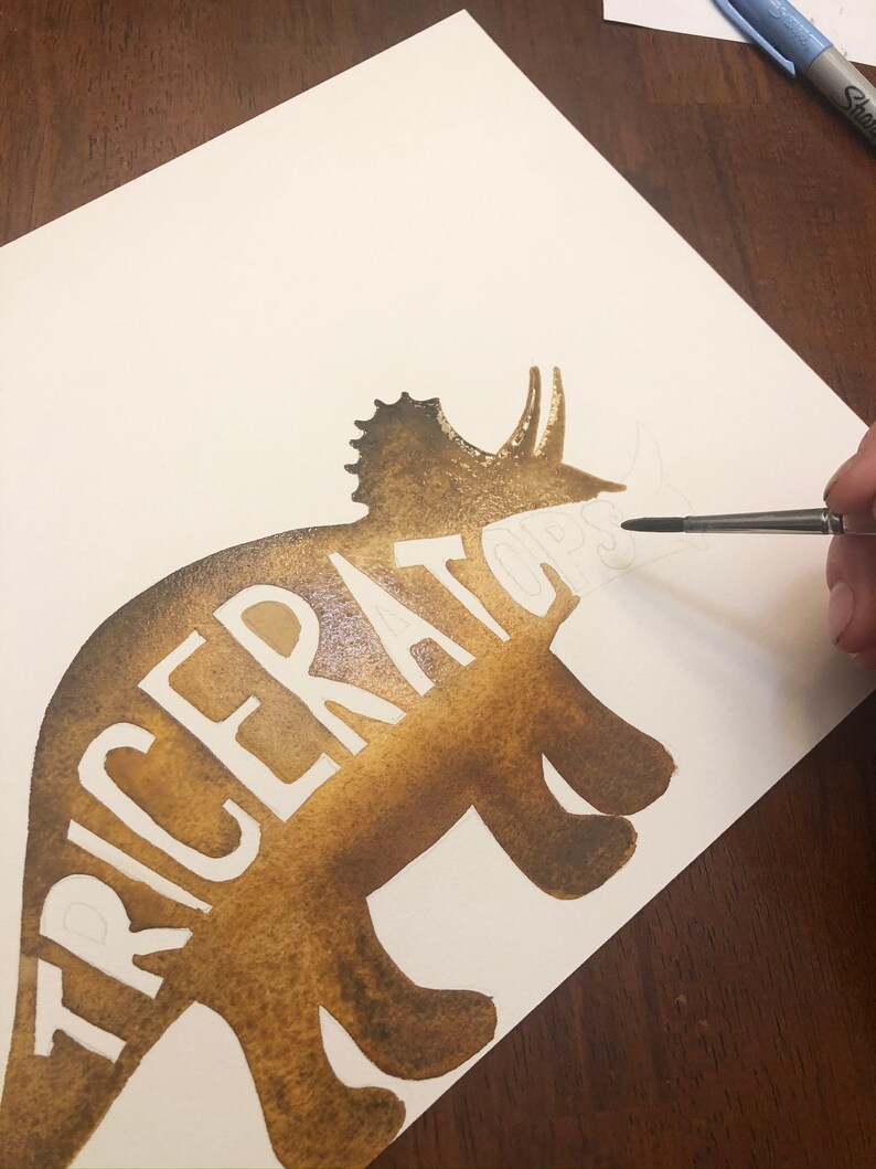 May include: A brown watercolor painting of a triceratops silhouette with the word "TRICERATOPS" written in white inside the silhouette.