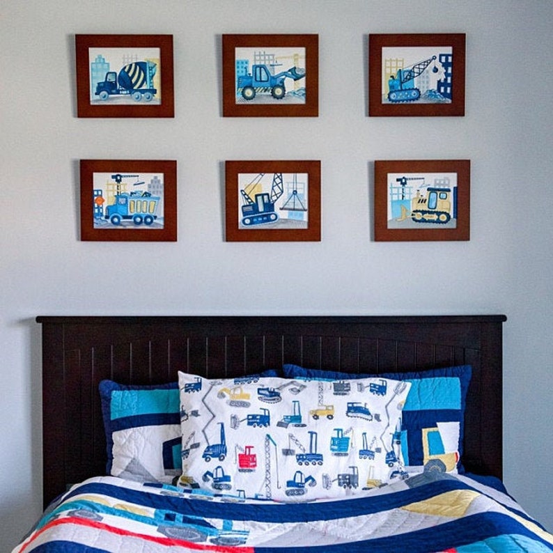Puede incluir: Una cabecera de cama de madera marr&oacute;n oscuro con un edred&oacute;n estampado en azul y blanco sobre una cama. La pared detr&aacute;s de la cama tiene seis cuadros enmarcados de veh&iacute;culos de construcci&oacute;n.