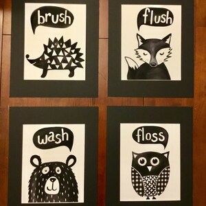 May include: Four black and white framed prints with animal illustrations and text bubbles. The prints read "brush" with a hedgehog, "flush" with a fox, "wash" with a bear, and "floss" with an owl.