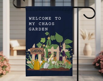 Może przedstawiać: Granatowa flaga ogrodowa z białym napisem "WELCOME TO MY CHAOS GARDEN". Flaga przedstawia scenę ogrodową z białym płotem, warzywami i narzędziami ogrodniczymi. Widoczna jest żółta konewka i łopata.