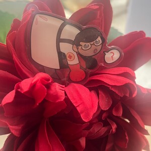 Può includere: Un fiore rosso con un adesivo a fumetto di una persona con occhiali e uniforme medica. L'adesivo ha un punto interrogativo e un simbolo della croce rossa.
