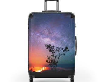 Puede incluir: Una maleta negra con una imagen vibrante de un cielo estrellado, una silueta de árbol y una puesta de sol ardiente. La maleta tiene un asa retráctil y cuatro ruedas para facilitar el transporte.