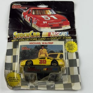Könnte beinhalten: Ein gelb-schwarzes NASCAR-Rennwagen-Spielzeug, Nummer 30, auf einem Präsentationsständer, verpackt mit einer Sammlerkarte. Die Verpackung zeigt eine rote Autografik, den Text "STOCK CAR" und "NASCAR".