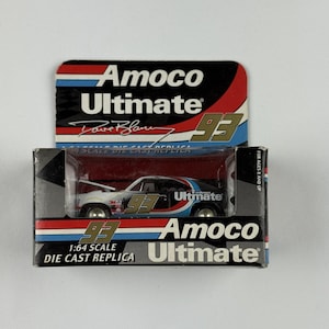Puede incluir: Réplica a escala 1:64 de un coche de carreras, con el logotipo de Amoco Ultimate y el número 93. El coche es negro, blanco y azul, con el nombre "Dave Blaney" visible. El embalaje incluye el logotipo de Amoco Ultimate.