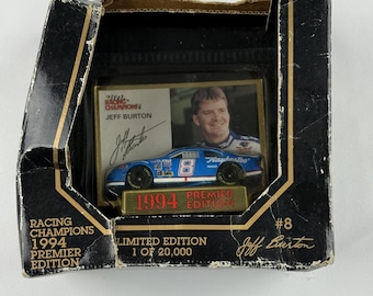 May include: A Racing Champions 1994 Premier Edition die-cast car of Jeff Burton, number 8, in its original box. The blue and white car is displayed on a gold stand. The box is black with gold accents and features the Racing Champions logo.