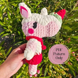 Puede incluir: Muñeca de unicornio de ganchillo hecha a mano en tonos blanco, rosa y rojo. El unicornio tiene una bufanda roja, una falda rosa y un cuerno con detalles verdes. El texto "PDF Pattern Only" es visible.