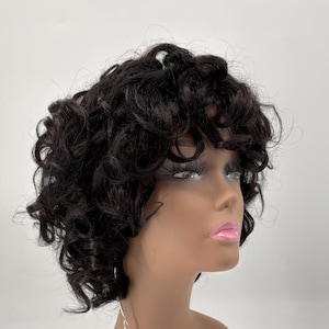 May include: A short, dark brown wig with tight, voluminous curls styled on a mannequin head. A pink, oval-shaped tag hangs from the neck, featuring the text "HUMAN HAIR GENERAL CARE" and detailed instructions for maintaining the hair piece.