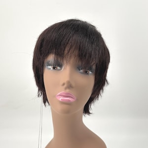 May include: A short, dark brown wig with straight, layered hair and bangs styled on a mannequin head. The wig features a natural-looking texture and is displayed with a white product care tag attached by a thin string to the side of the head.