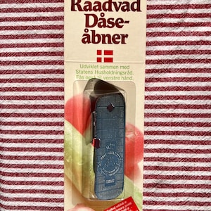 May include: A blue Raadvad can opener in its original packaging. The packaging features the text "Raadvad Dåse-åbner" and the number "1499". The background is a red and white striped pattern.