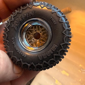 May include: A black rubber tire with a deep tread pattern mounted on a gold-colored metal wheel with a chrome rim. The tire sidewall features the text INJORA, XXPIN, T1022, and 60x20mm-R1.0 molded into the surface of the rubber material.