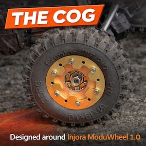 Puede incluir: Primer plano de un neumático negro con una rueda dorada y cobriza en forma de engranaje. El neumático tiene un dibujo de banda de rodadura rugoso. El texto de la imagen dice "THE COG" y "Designed around Injora ModuWheel 1.0".