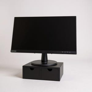 May include: A black Lenovo computer monitor on a black monitor stand with two small drawers. The monitor has a black screen and a black base. The stand is made of wood and has a circular base.