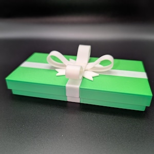 May include: A bright green gift box with a white ribbon and bow. The box has a rectangular shape with a white ribbon wrapped around it. The bow is centered on top of the box.