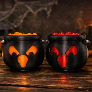 May include: Two black plastic cauldrons with cut-out facial features. The left cauldron has orange interior lighting and is filled with orange spheres. The right cauldron has red interior lighting and is filled with red spheres. Both have handles.