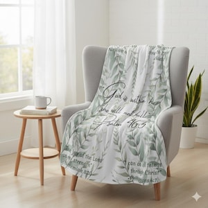 May include: A white throw blanket draped over a gray armchair. The blanket features a watercolor design of green leaves and script text that reads "God is within her, she will not fall" and other Bible verses.