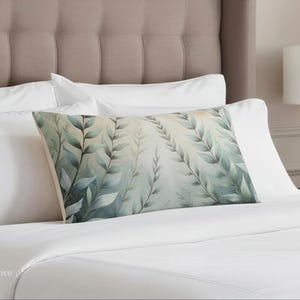 May include: A rectangular decorative pillow with a watercolor design of green leaves and branches. The pillow is placed on a bed with white sheets and pillows. The headboard is a neutral color.