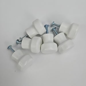 May include: A collection of seven white ceramic cabinet knobs with silver screws. The knobs have a rounded, mushroom-like shape, suitable for drawers or cabinets. The hardware is set against a plain white background.