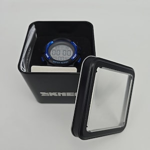 May include: A digital watch with a blue bezel and black band is displayed inside a black box. The watch face shows the time and date. The box has the brand name "SKMEI" printed on it. The watch is water resistant.