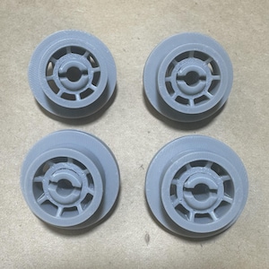 May include: Four gray, 3D-printed wheels with a central hub and a circular design. The wheels have a layered construction with a series of spokes radiating from the center. The wheels are arranged in a square formation.