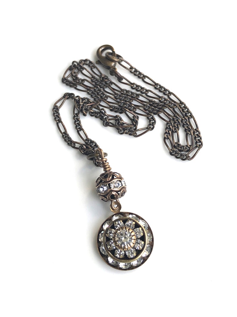 Art deco styled necklace with antique brass figaro chain with a Swarovski clear crystal ball attached to a 15mm brilliant Swarovski clear crystal three tiered disc with one large Swarovski crystal in the center. Choose from 16, 18 or 20 inch chain.