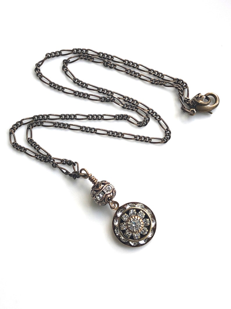 Art deco styled necklace with antique brass figaro chain with a Swarovski clear crystal ball attached to a 15mm brilliant Swarovski clear crystal three tiered disc with one large Swarovski crystal in the center. Choose from 16, 18 or 20 inch chain.