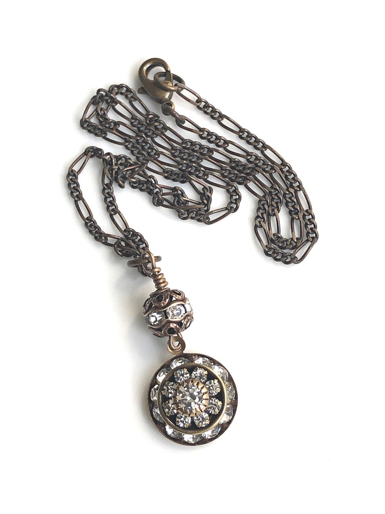 Art deco styled necklace with antique brass figaro chain with a Swarovski clear crystal ball attached to a 15mm brilliant Swarovski clear crystal three tiered disc with one large Swarovski crystal in the center. Choose from 16, 18 or 20 inch chain.