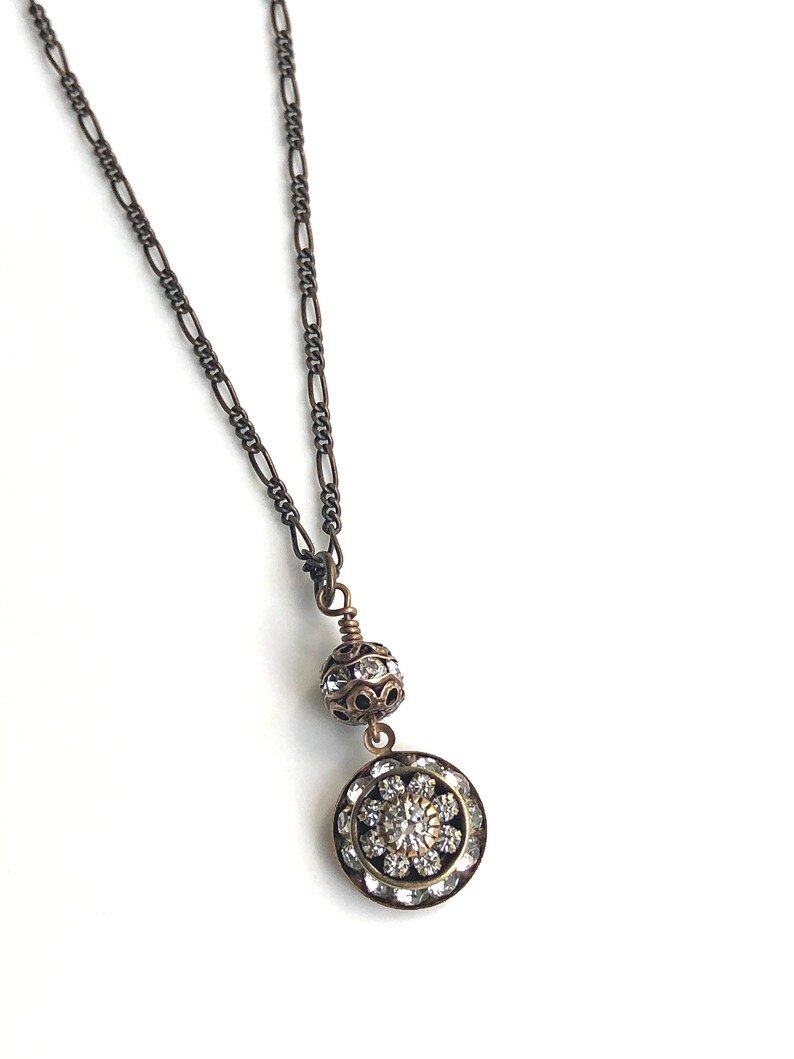 Art deco styled necklace with antique brass figaro chain with a Swarovski clear crystal ball attached to a 15mm brilliant Swarovski clear crystal three tiered disc with one large Swarovski crystal in the center. Choose from 16, 18 or 20 inch chain.