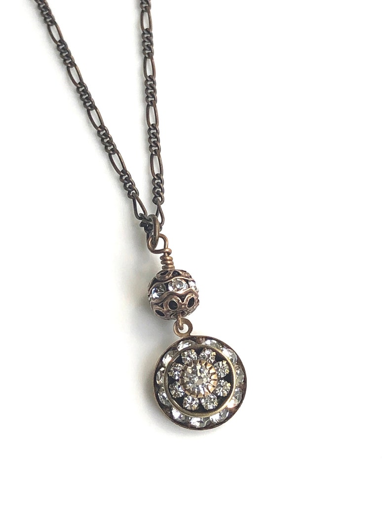 Art deco styled necklace with antique brass figaro chain with a Swarovski clear crystal ball attached to a 15mm brilliant Swarovski clear crystal three tiered disc with one large Swarovski crystal in the center. Choose from 16, 18 or 20 inch chain.