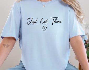 May include: A light blue t-shirt with the handwritten text "Just Let Them" and a heart symbol. The shirt has short sleeves and a relaxed fit, suitable for casual wear.