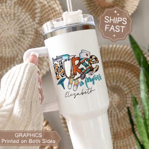 Pode incluir: Caneca branca com alça, com um design colorido "NURSE in progress". O design inclui símbolos médicos como uma seringa, um estetoscópio e um chapéu de enfermeira. O nome "Elizabeth" está escrito abaixo. A caneca tem uma tampa transparente e um canudo.