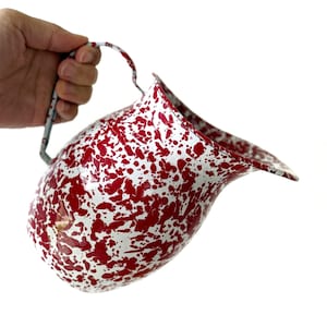 May include: A vintage-style enamelware pitcher with a red and white speckled pattern. The pitcher has a curved spout and a handle. The overall design is reminiscent of classic kitchenware.