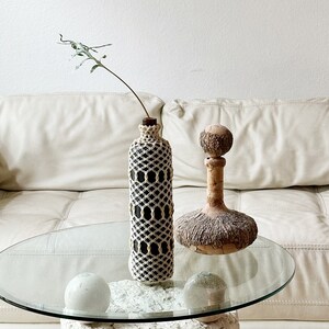 May include: A white couch with a glass coffee table with a white stone base. On the table are two decorative bottles, one with a black and white crocheted cover and the other with a brown, textured surface.
