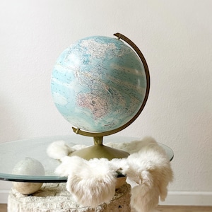 May include: A vintage globe with a blue and white map on a gold stand, sitting on a glass table with a white faux fur throw draped over it.