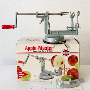 May include: An Apple-Master apple parer, corer, and slicer with a red handle. The kitchen tool is silver-colored and sits on a box with the product name and images of apples. Includes a vacuum base and extra mounting clamp.