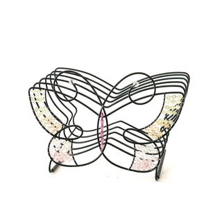 May include: A black wire butterfly-shaped rack featuring decorative accents of small, multi-colored beads in shades of pink, yellow, and clear. The structure is composed of curved metal wires forming the wings and body of the butterfly.