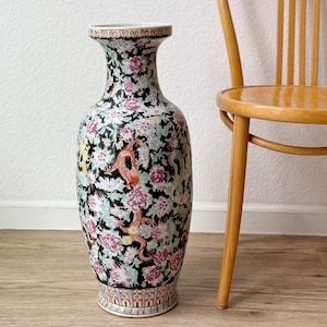 May include: A tall, decorative ceramic vase with a black background and a floral and dragon design. The vase features pink, white, and green flowers, and a red dragon. The vase is approximately 24 inches tall.